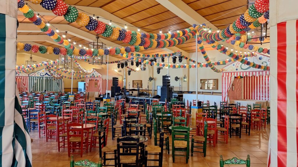 una feria de abril exclusiva para empresa montada en interior con farolillos y sillas y mesas típicas sevillanas.